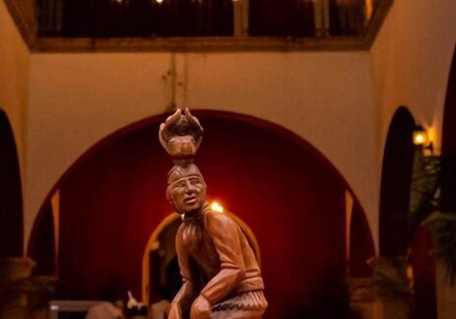 A statue in a dimly lit room with a red archway in the background.