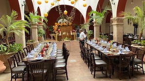 Un amplio comedor interior con numerosas mesas y sillas, rodeado de columnas y plantas en macetas.