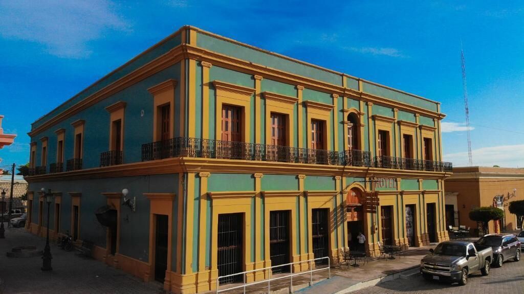 Un edificio de dos pisos con un balcón en el segundo nivel, una entrada visible y un letrero que indica que es un hotel.