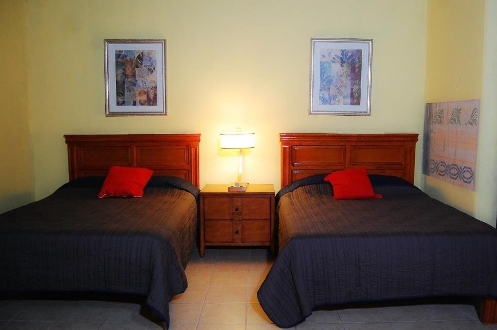 Een hotelkamer met twee bedden, een nachtkastje met lamp en lijstwerken aan de wanden.