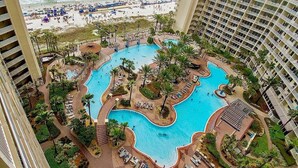 Een hotel met een groot, onregelmatig zwembad omringd door palmbomen en ligbedden, met uitzicht op een strand.