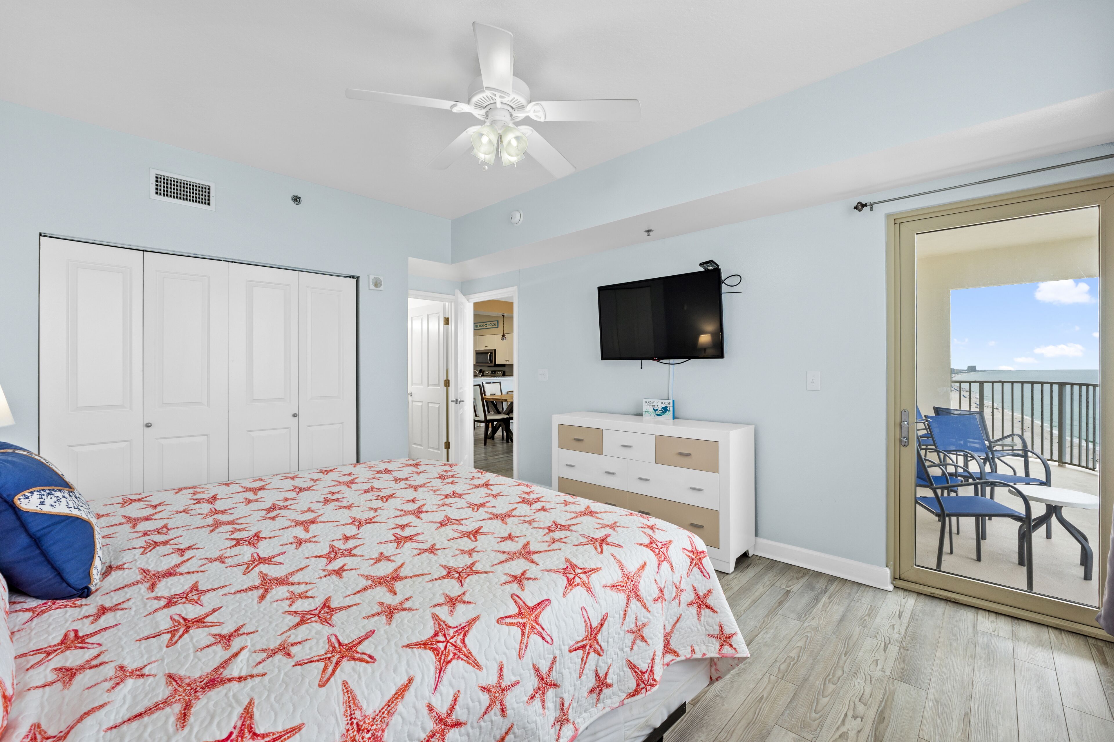 Une chambre avec un lit, un ventilateur de plafond, une télévision et un balcon équipé de chaises.