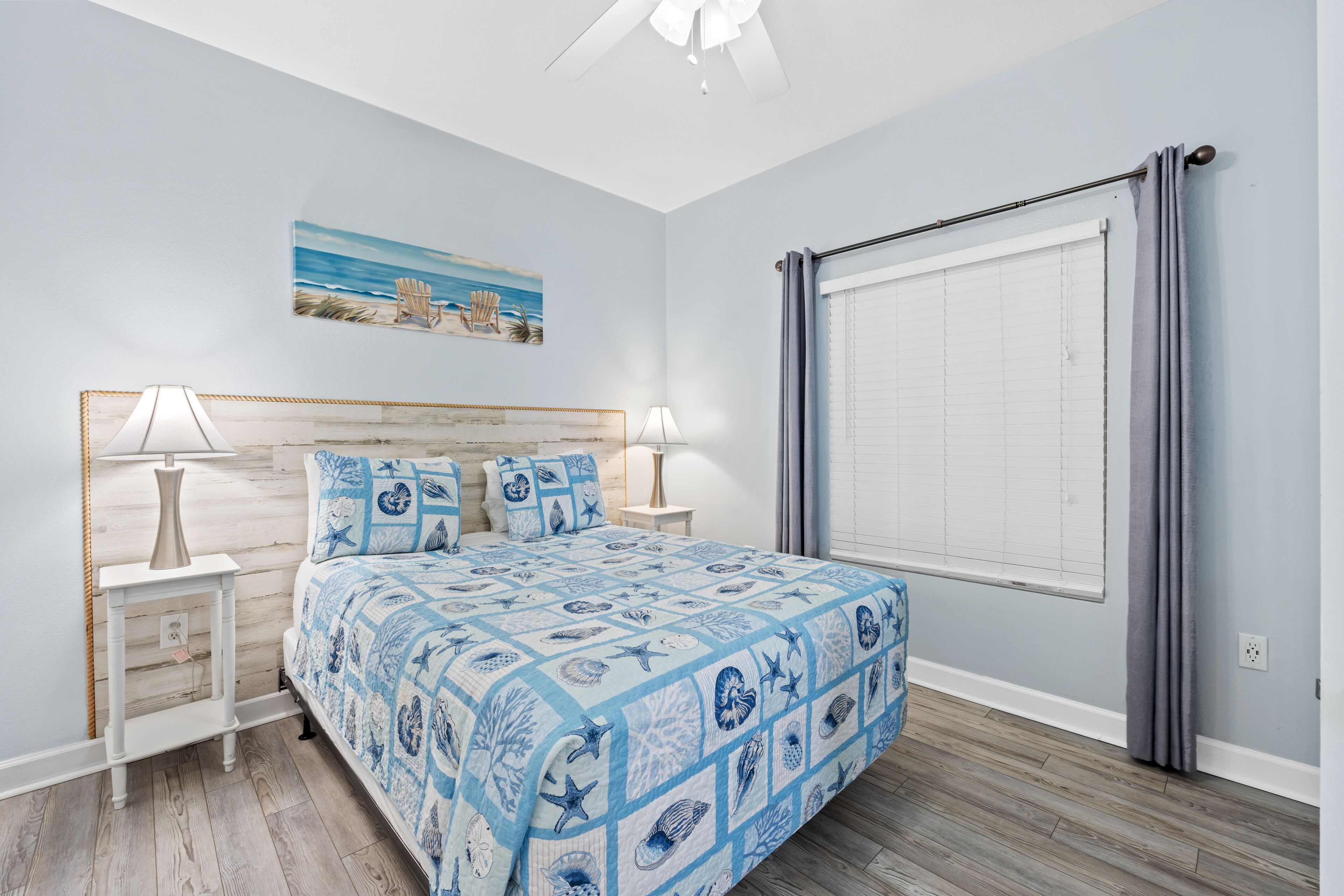 A bedroom with a bed, two bedside tables, a ceiling fan, a window with curtains, and a painting on the wall.