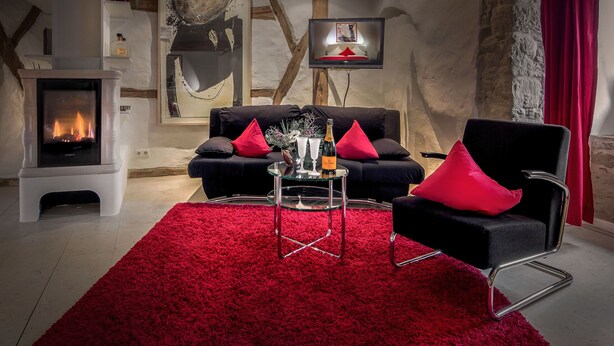 A cozy living room with a fireplace, a sofa, and a red carpet. - Edelzimmer Rothenburg (Rothenburg ob der Tauber)