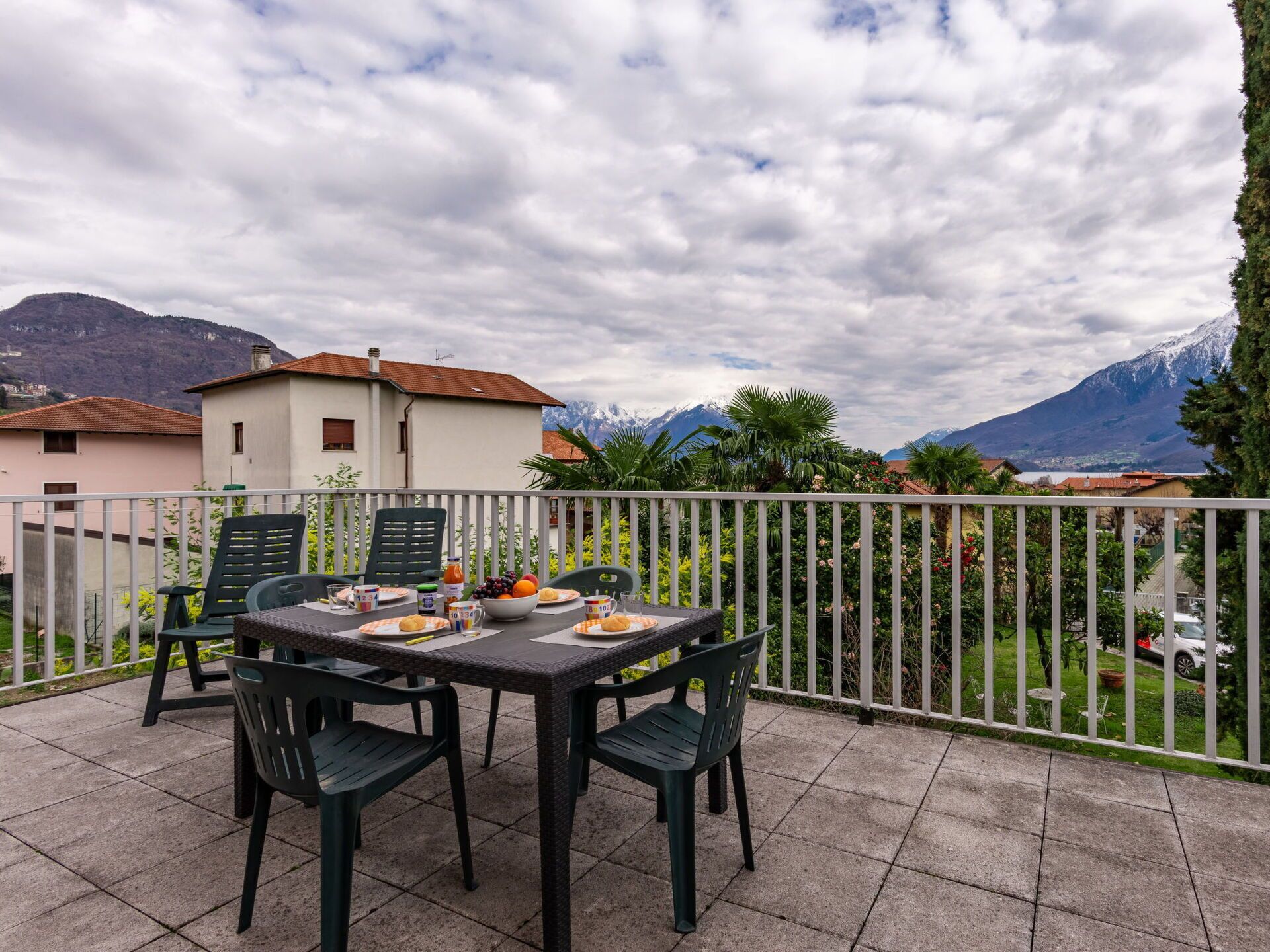 An outdoor patio with a table set for dining, surrounded by chairs, overlooking a mountainous landscape.