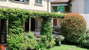 A two-story building with a garden area featuring a variety of plants and a decorative fountain. - Lovely apartment for 5 people with WIFI, TV, terrace and pets allowed (Dongo)