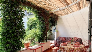 A balcony with a table set for dining, surrounded by potted plants and a red metal chair. - Lovely apartment for 5 people with WIFI, TV, terrace and pets allowed (Dongo)