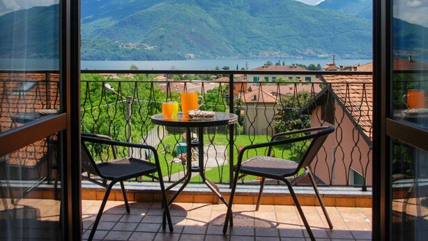 En balkon med to stole og et lille bord, med udsigt over et bjerglandskab med en sø og bygninger i det fjerne.