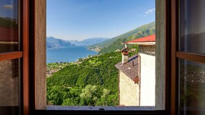 A view from a window overlooking a mountainous landscape with a lake, a small building with a red roof, and lush greenery. - Beautiful private villa for 4 guests with WIFI, TV, patio and pets allowed (Peglio)