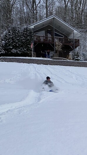 A person sledding down a snowy slope with a building in the background.