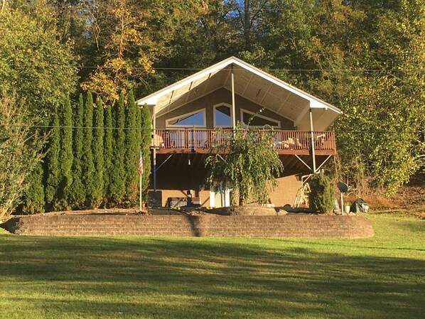 A two-story house with a balcony, surrounded by trees and a grassy yard.