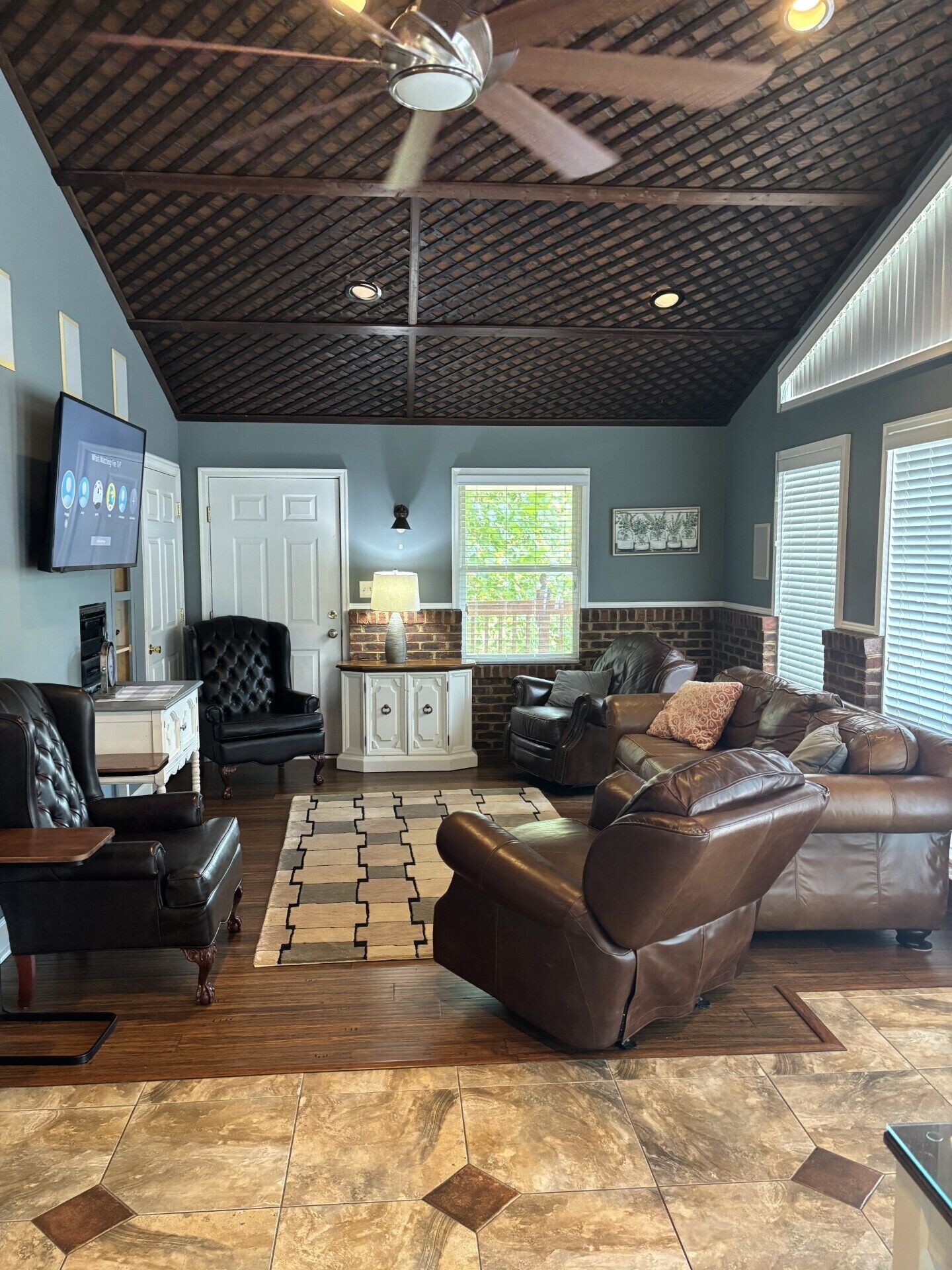A spacious living room with a high ceiling, a fireplace, leather sofas, and a television mounted on the wall.