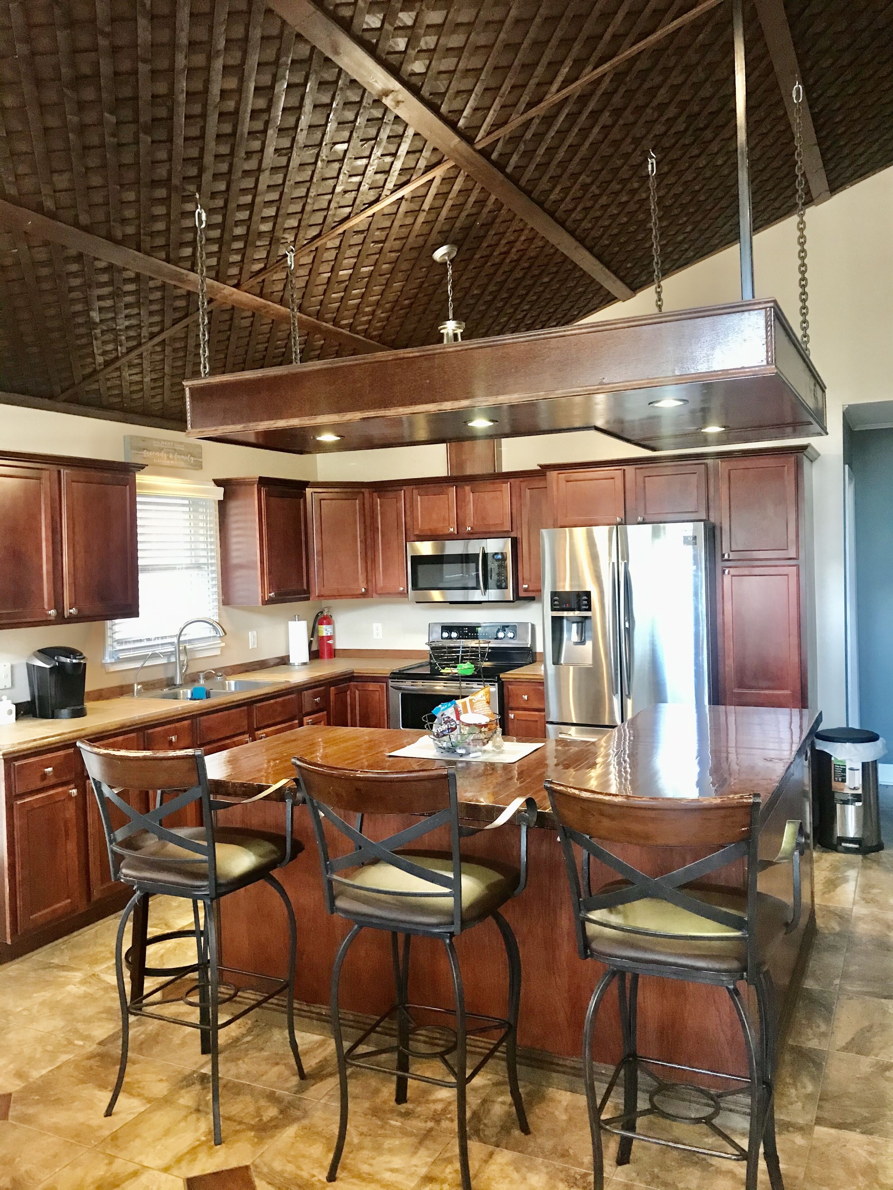 A modern kitchen with wooden cabinets, stainless steel appliances, and a bar area with stools.