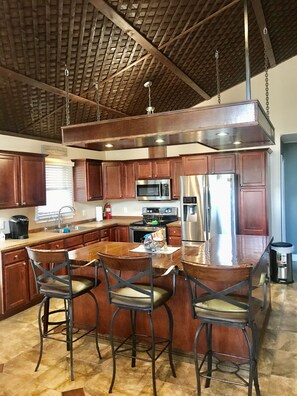 A modern kitchen with wooden cabinets, stainless steel appliances, and a bar area with stools.