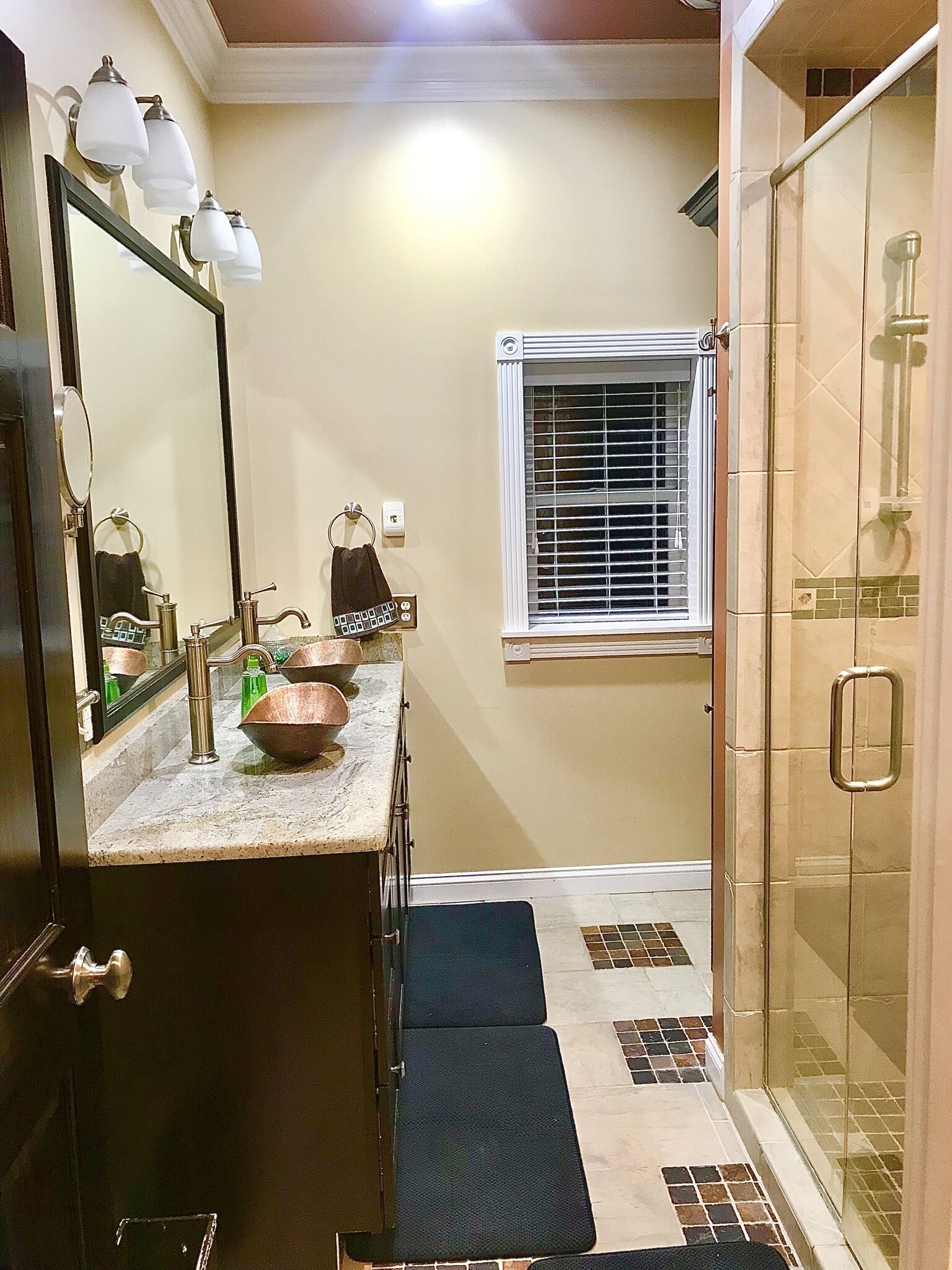 A bathroom with a large mirror, a sink with copper fixtures, a towel rack, and a shower area.