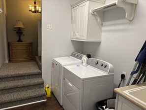 A laundry room with a front-loading washer and dryer, a wooden dresser, and a staircase leading to another room.