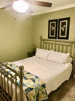 A bedroom with a metal bed frame, a quilt, a ceiling fan, and two framed pictures on the wall.