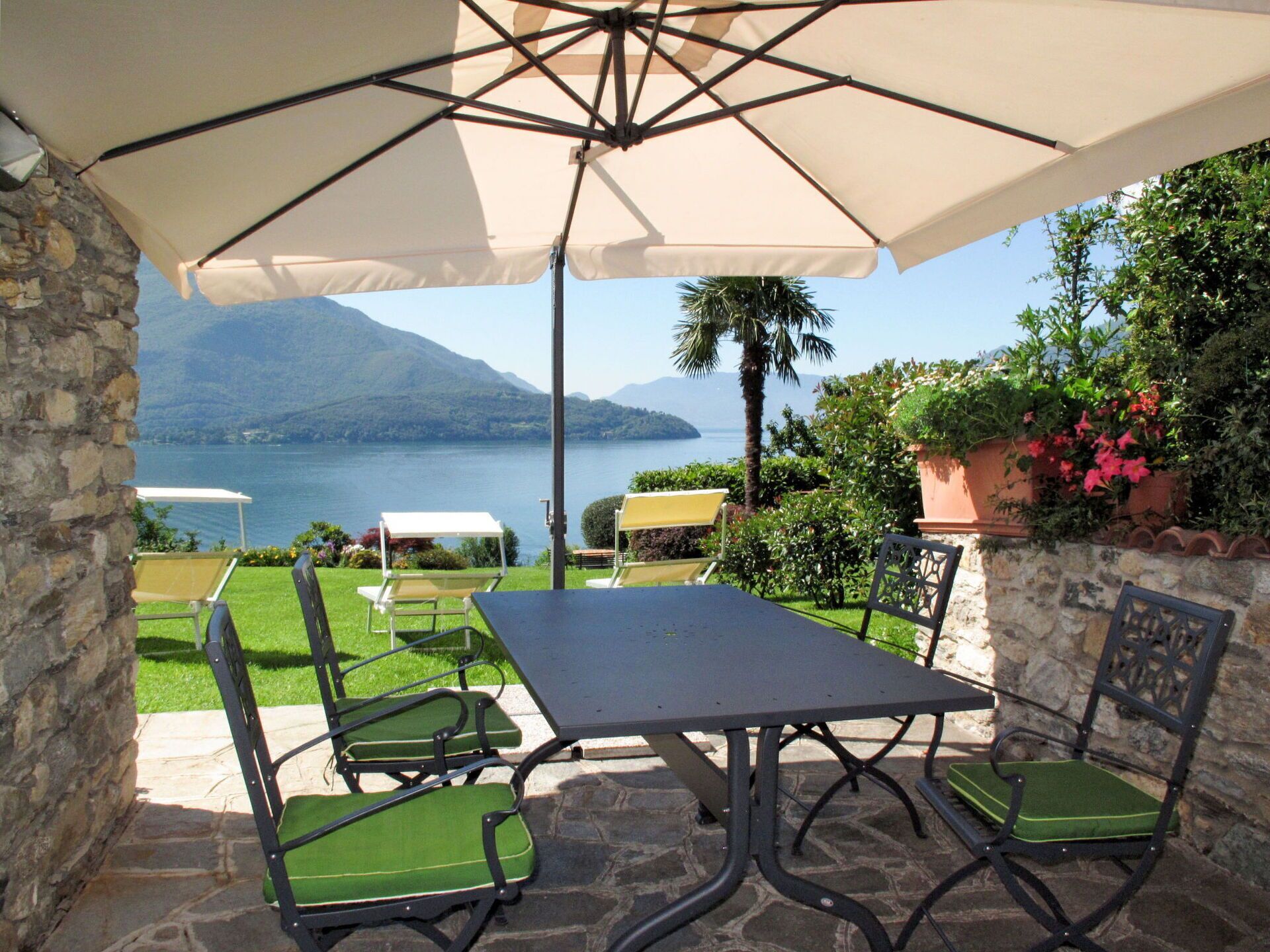 An outdoor patio with a table and chairs, a large umbrella, and a view of a lake and mountains.