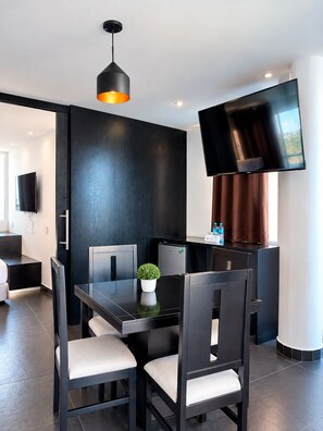 Een moderne eetruimte met een zwarte tafel en stoelen, een potplant, een flatscreen televisie aan de muur en een schuifdeur naar een andere kamer.