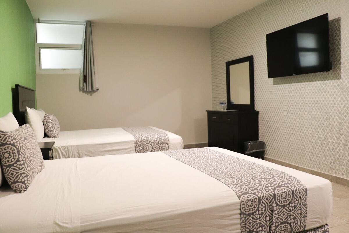 A hotel room with two beds, a TV, a dresser, and a window.