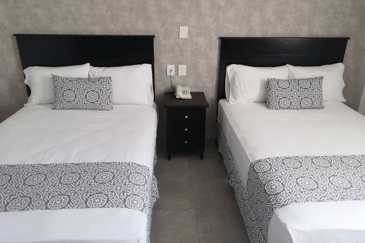 Two twin beds with patterned bedding, a bedside table with a phone, and a wall socket.