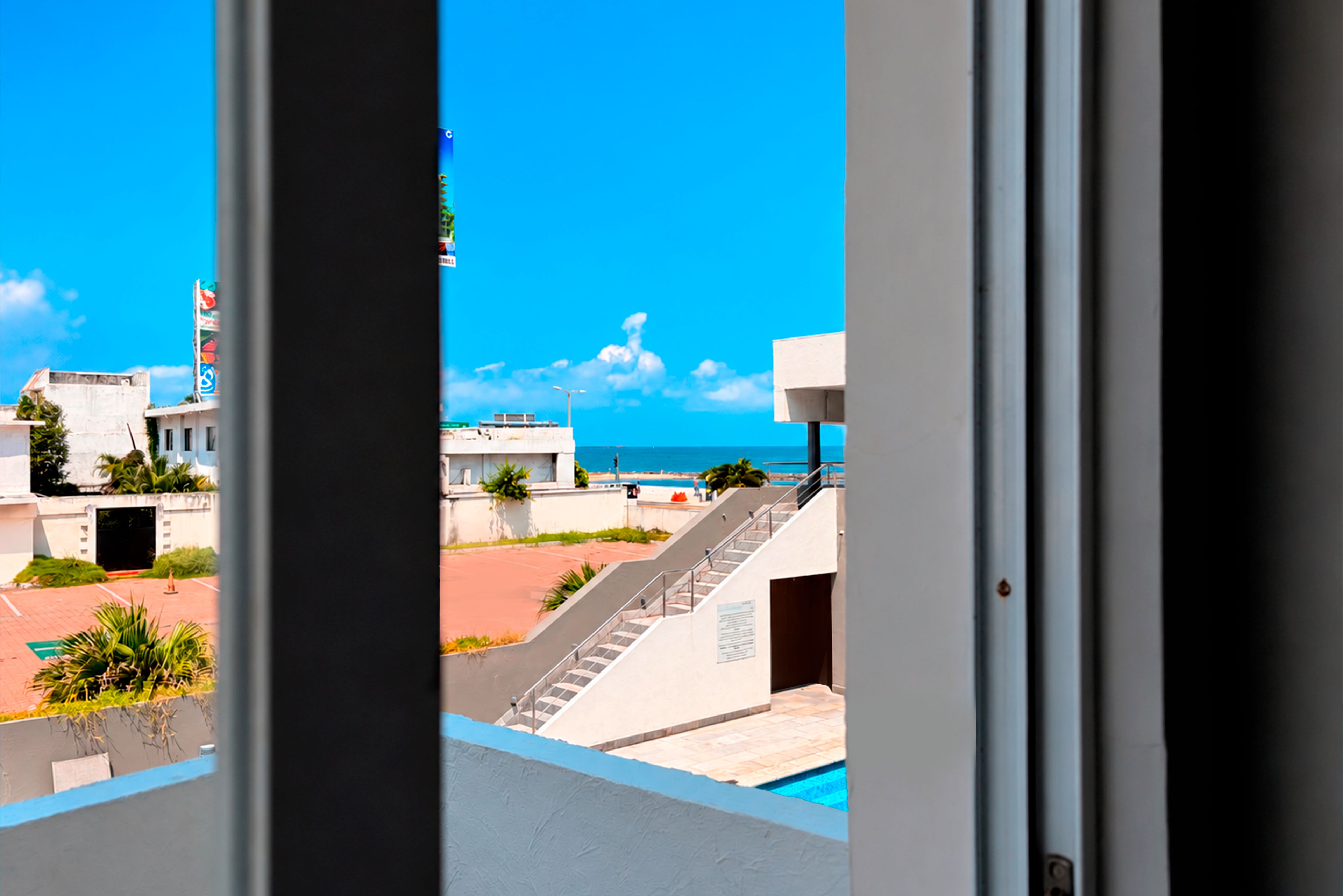 Vista desde una ventana con vista a una piscina, una escalera y un cielo azul despejado.
