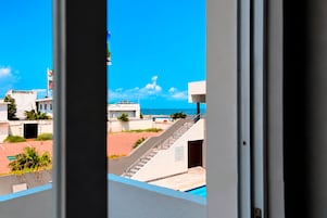 Vista desde una ventana con vista a una piscina, una escalera y un cielo azul despejado.