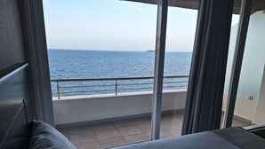 A hotel room with a large window overlooking the sea, a balcony with a railing, and a bed with patterned pillows. - Hotel Costa Verde (Veracruz)