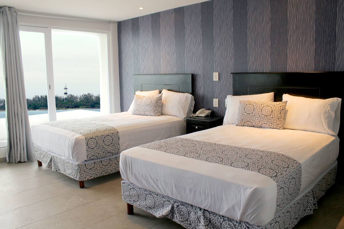 A hotel room with two beds, a large window, and a view of a lighthouse.