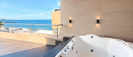 Un baño moderno con una bañera grande, un balcón con vista al mar y dos luces empotradas.