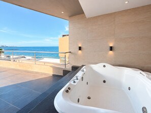 Un baño moderno con una bañera grande, un balcón con vista al mar y dos luces empotradas.