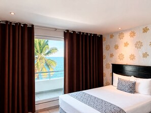Een hotelkamer met een bed, gordijnen, uitzicht op zee en een behang met een patroon.