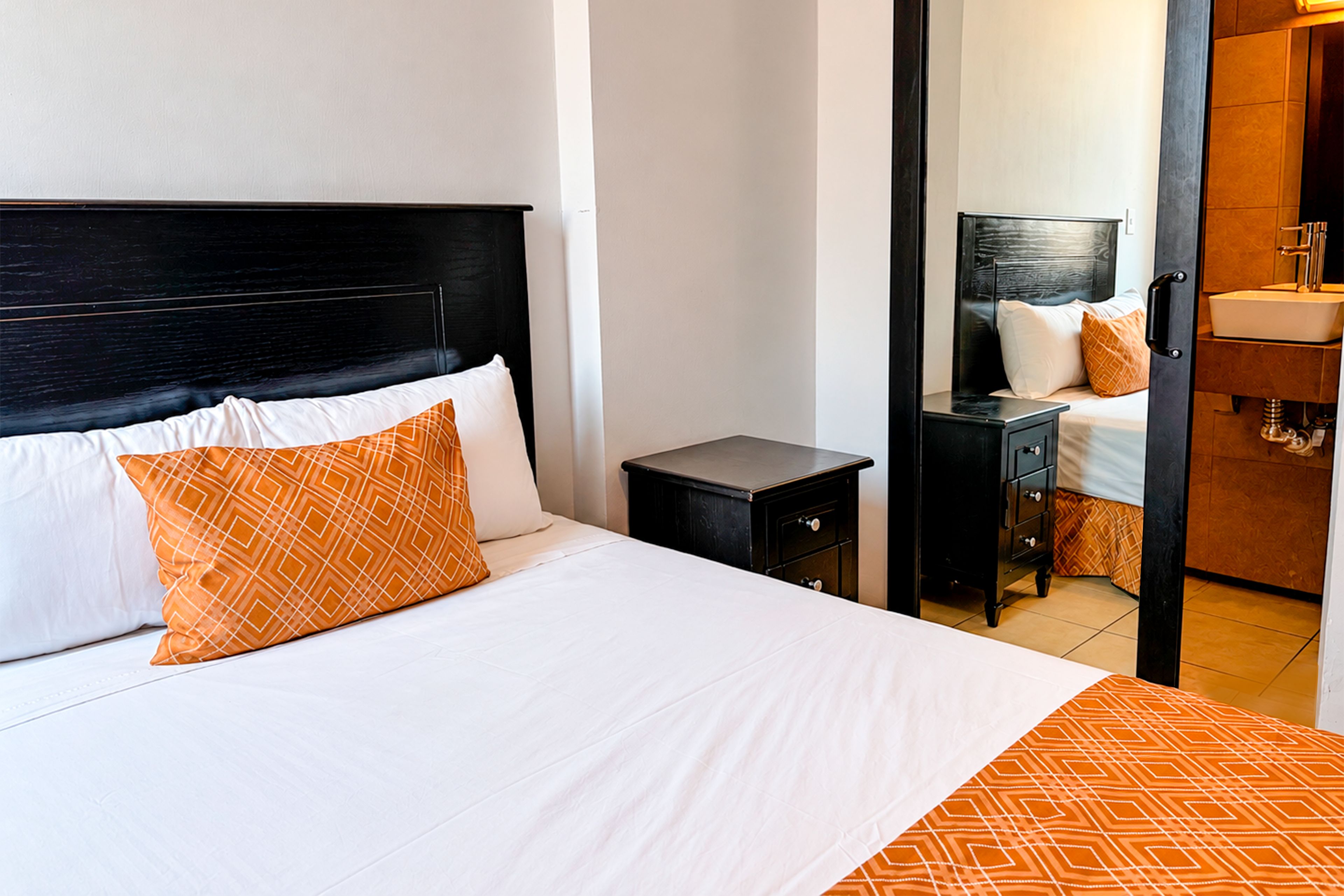 Habitación de hotel con cama, mesita de noche, cómoda y espejo.