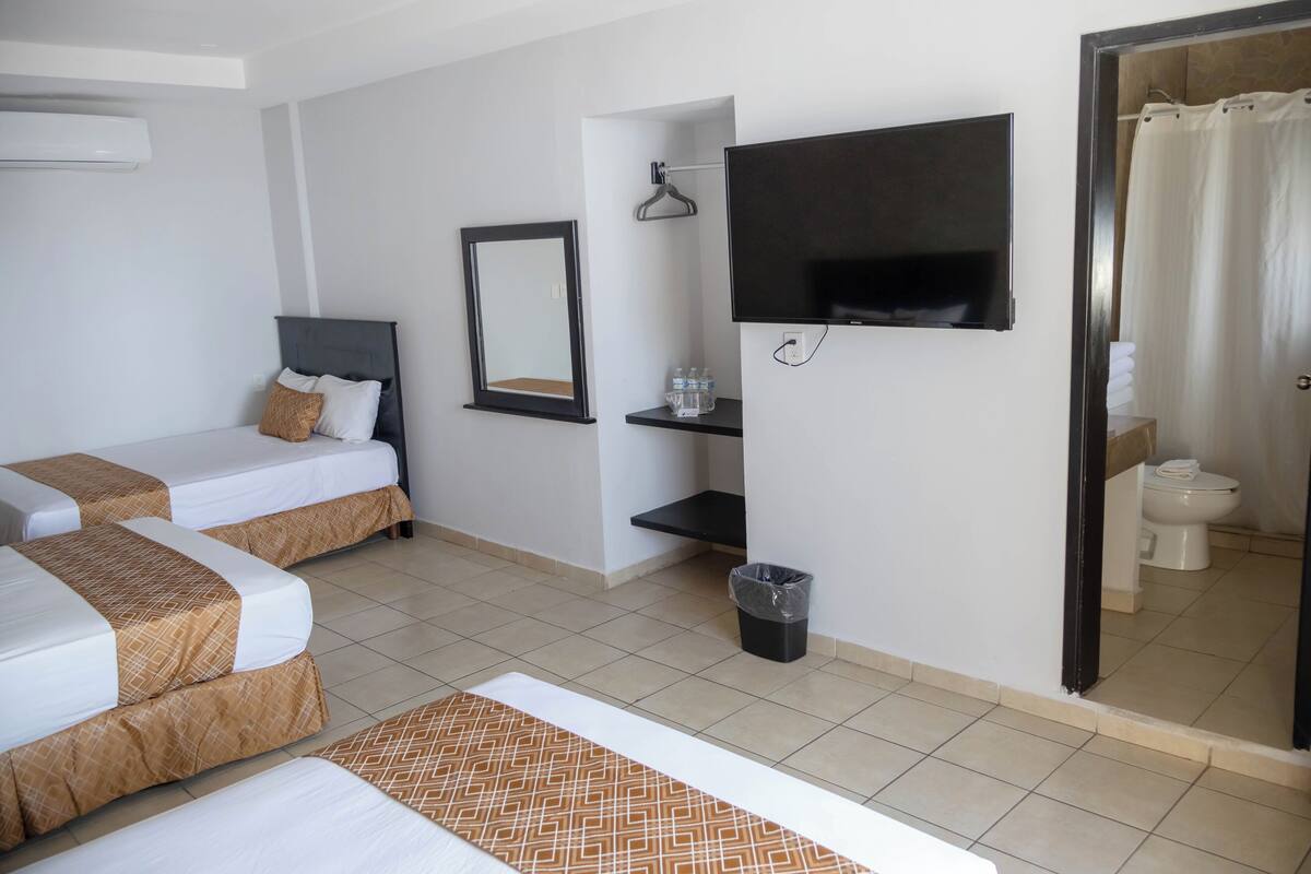A hotel room with two beds, a TV, a mirror, a shelf with toiletries, and a bathroom visible through an open door.
