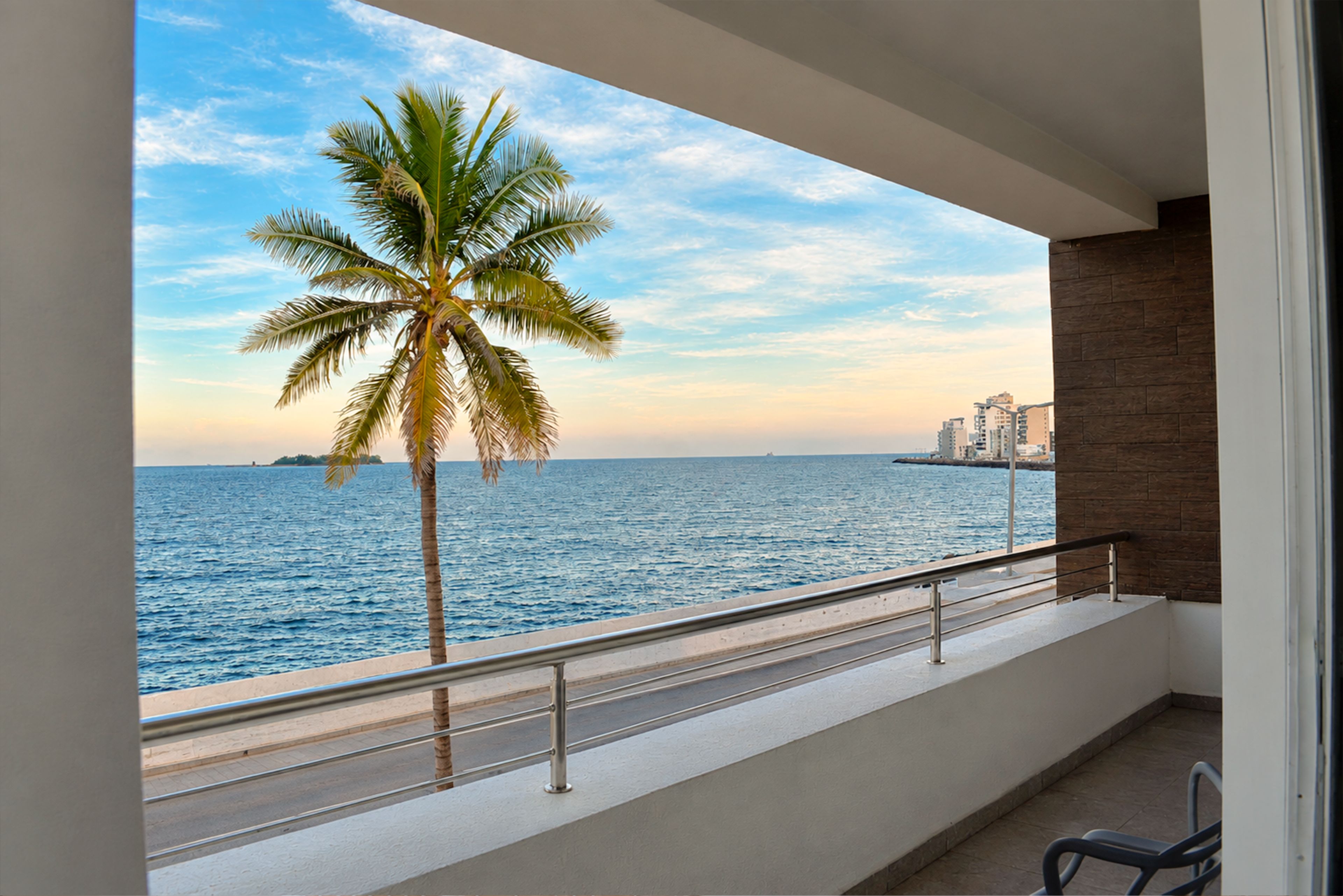 A balcony with a view of the sea and a palm tree.