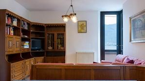 A cozy living room with a wooden cabinet, a television, a radiator, a sofa, and a window with a view. - Beautiful apartment for 9 guests with hot tub, WIFI, TV, patio and pets allowed (Aurogna)