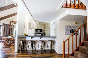 A modern kitchen with a bar area, wooden flooring, and a staircase.