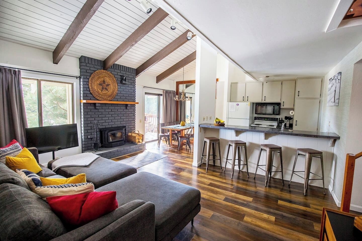 A modern living room with a fireplace, a dining area, and a kitchen with bar stools.