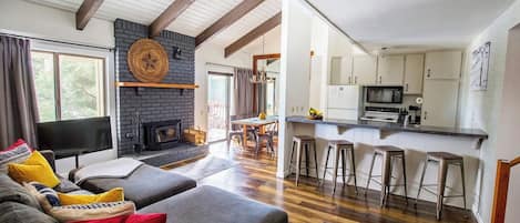 A modern living room with a fireplace, a dining area, and a kitchen with bar stools.