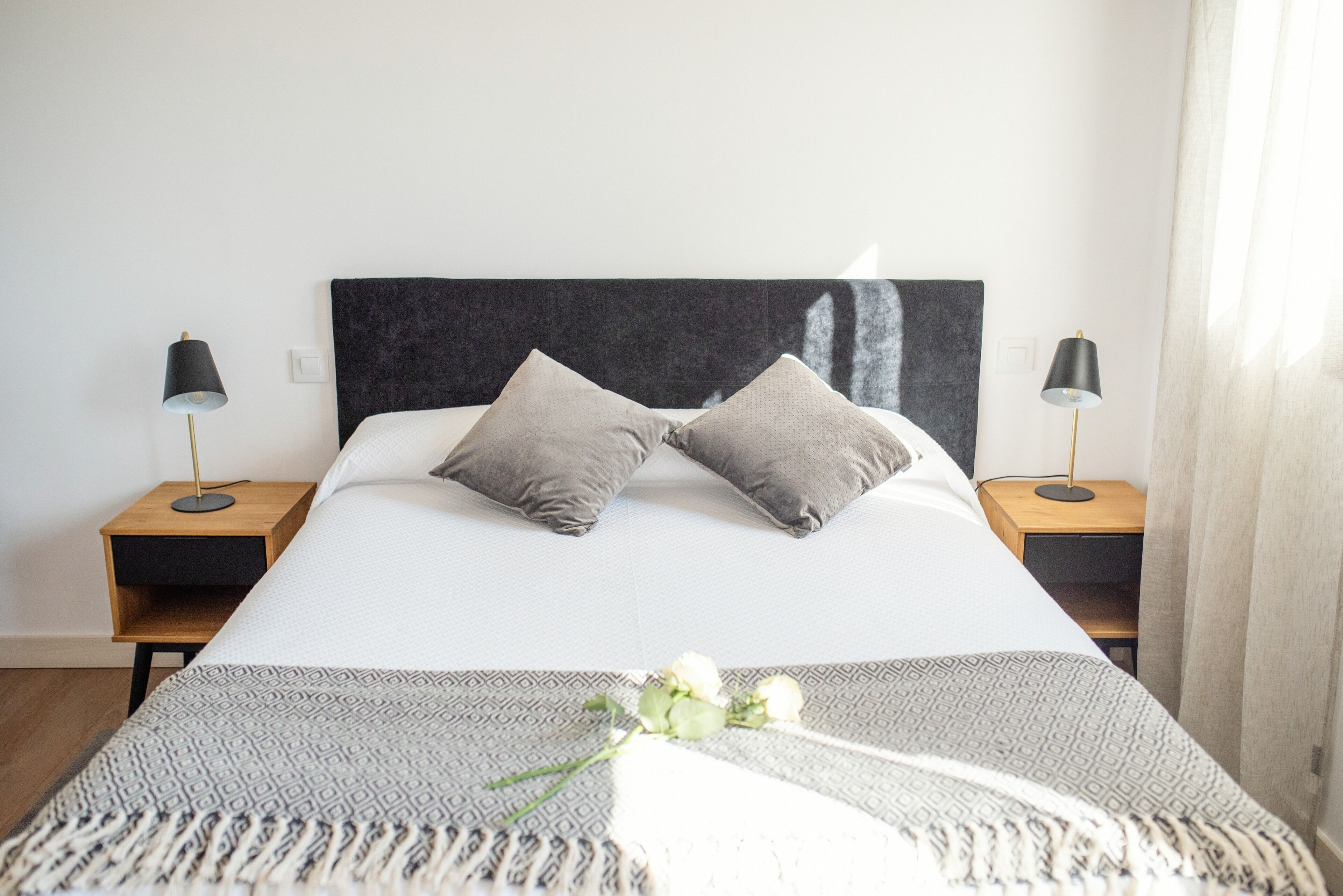 A neatly made bed with a patterned bedspread, two pillows, and a bedside table with a lamp.