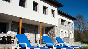A building with a stone facade, a covered patio area with blue lounge chairs, and a clear blue sky. - Pico El Hayal - Apar located in a rural setting with 2 bedrooms, kitchen, living room and bathroom (Ampuero)