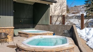 Two hot tubs with stone surrounds, a stone bench, and a metal chair. - Charming Studio + Loft Condo | Walk to Gondola | Pool, Hot Tubs and Views! (Steamboat Springs)