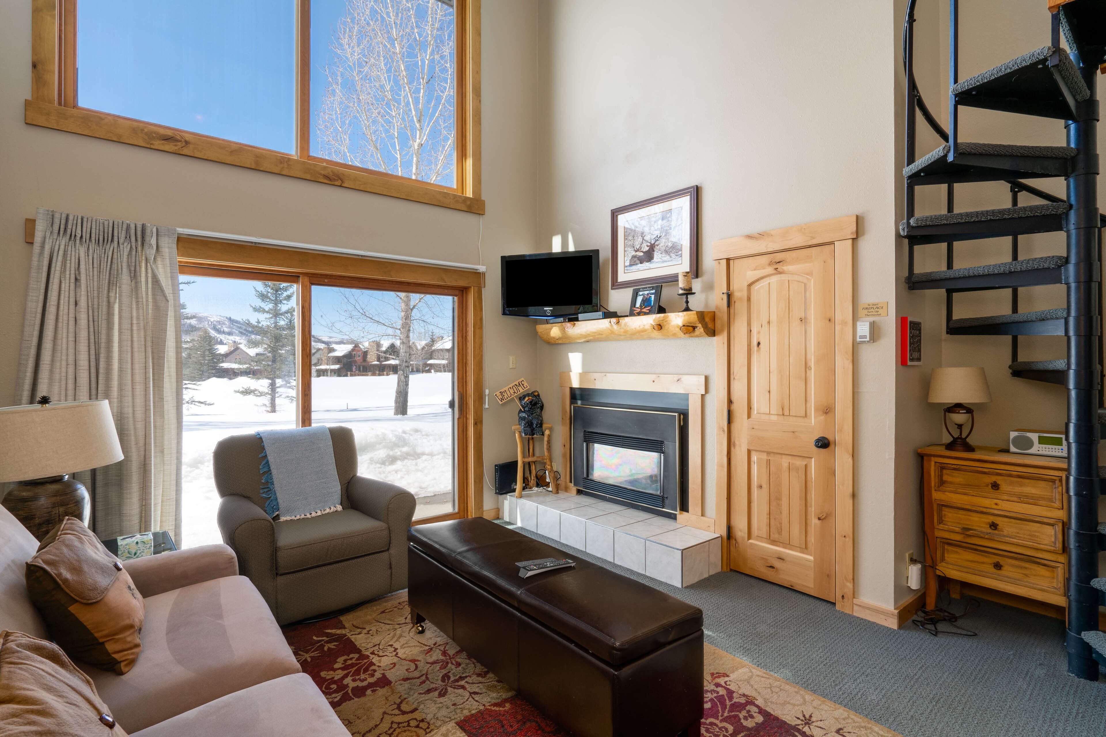A cozy living room with a fireplace, a television, and a view of the outdoors.