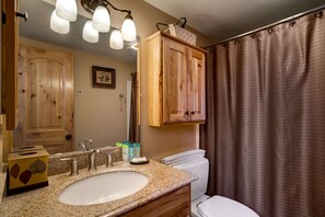 Un baño con tocador de madera, lavamanos, inodoro y cortina de ducha.