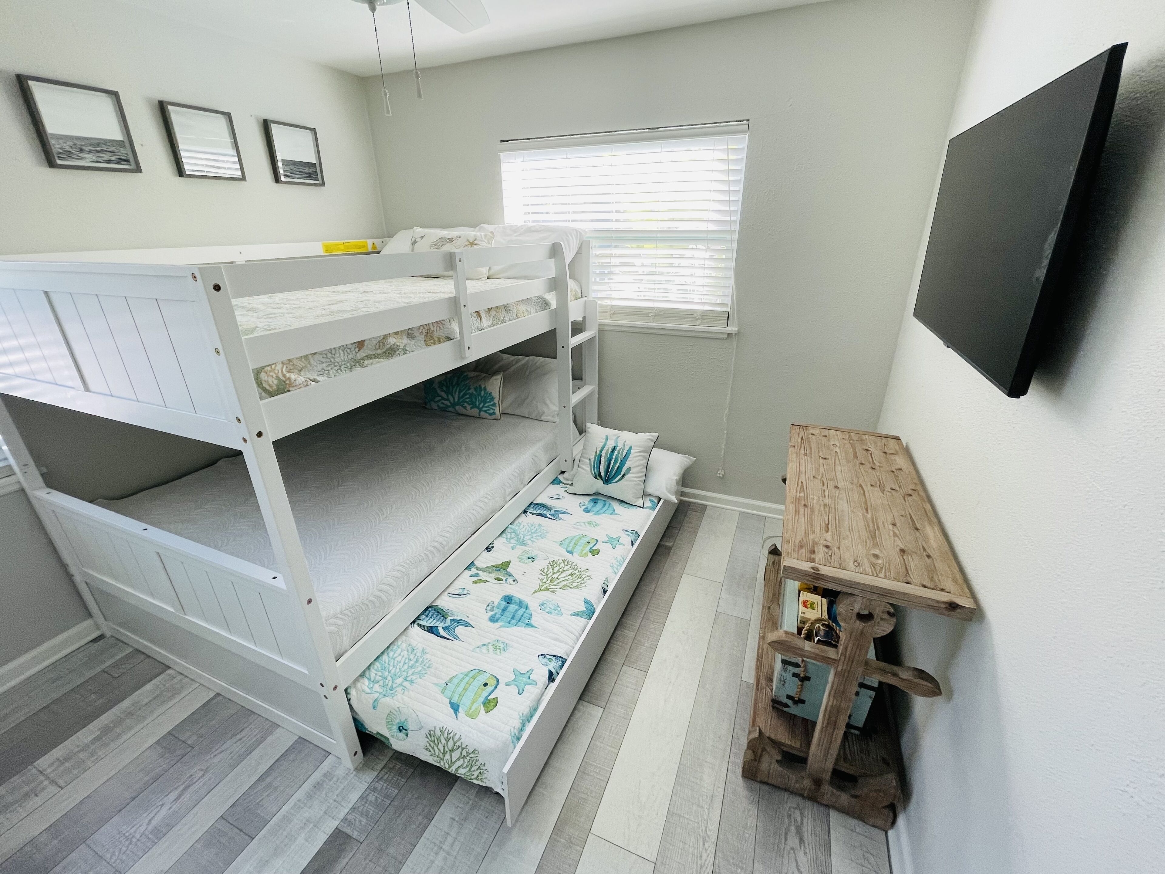 A bunk bed room with a wooden desk and a window with blinds.