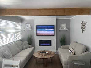 A living room with a beige sofa, a round coffee table, and a flat-screen TV mounted on the wall. - PRIVATE BEACH HOUSE W/PRIVATE POOL, 300ft TO BEACH ON THE SAND! SLEEPS 8! (Indian Shores)