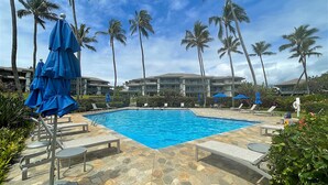 A swimming pool with lounge chairs and umbrellas, surrounded by palm trees and a hotel building. - Deluxe Ocean View Ground Floor.... Renovated ..Walk to the Hyatt and Beach...A/C (Koloa)