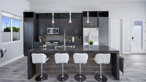 A modern kitchen with dark cabinetry, stainless steel appliances, and a central island with bar stools. - Modern Escape, La Quinta Cove #259116, 4 BR (La Quinta)