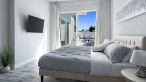 A modern bedroom with a bed, a TV mounted on the wall, and a view of a swimming pool through an open door. - Modern Escape, La Quinta Cove #259116, 4 BR (La Quinta)