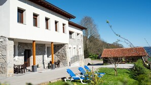 A two-story building with a stone facade and a flat roof. There are outdoor seating areas with tables and chairs, and a row of blue lounge chairs in the foreground. - Pico Rubia, two bedroom apartment, living room, kitchen and bathroom (Ampuero)